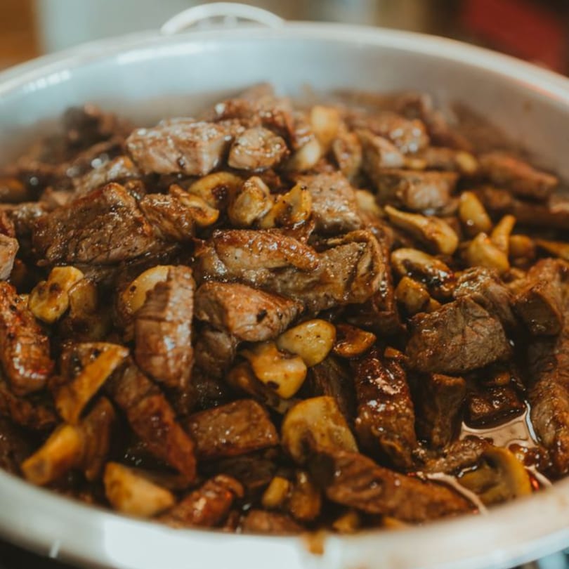 Close-up of sizzling beef and mushrooms in a white serving dish at Sushi World by Oishii.