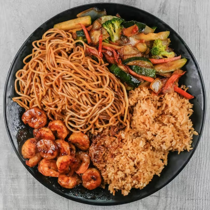 A black plate with shrimp, noodles, fried rice, and stir-fried vegetables.