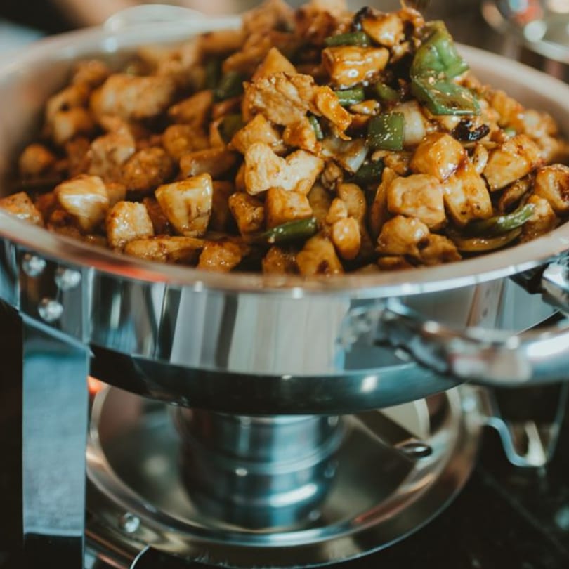 A chafing dish filled with stir-fried chicken, green peppers, and onions, ready to be served.