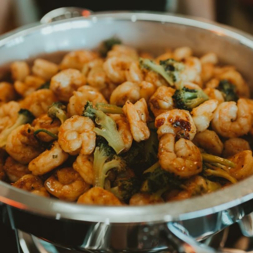 Close-up of shrimp and broccoli stir-fry in a metal serving dish at Sushi World by Oishii.