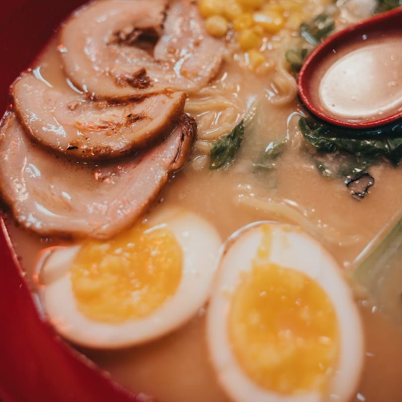 Close-up of a ramen bowl with pork, corn, green onions, and two soft-boiled eggs.